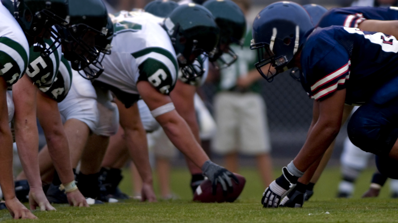 Football players lined up at the line of scrimmage, illustrating the neuroscience of athlete mental health, focus under pressure, and nervous system regulation.