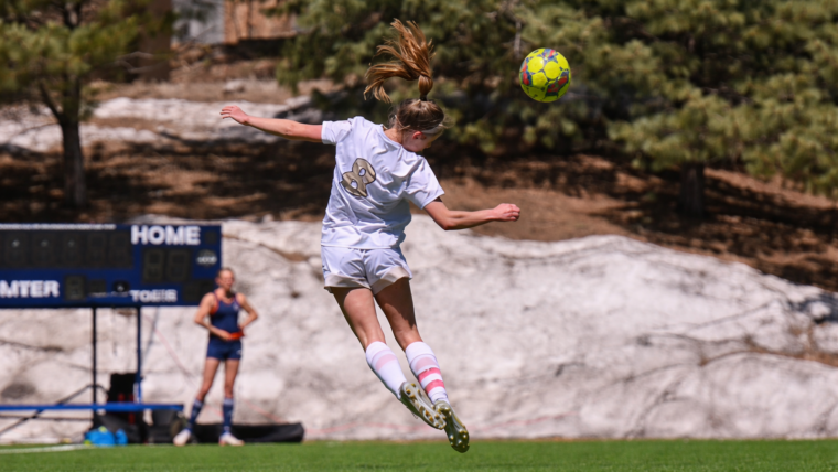 Young soccer athlete jumping to head the ball during a match, representing the challenge of returning to sport after injury and overcoming fear of reinjury